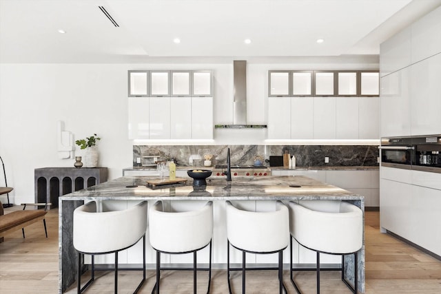 kitchen featuring appliances with stainless steel finishes, tasteful backsplash, white cabinetry, a kitchen bar, and wall chimney exhaust hood