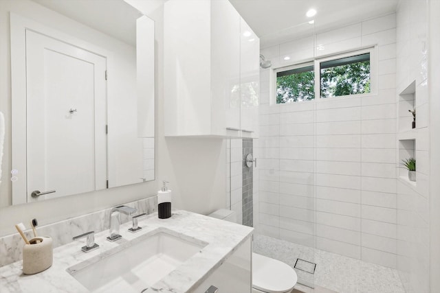 bathroom featuring vanity, a tile shower, and toilet