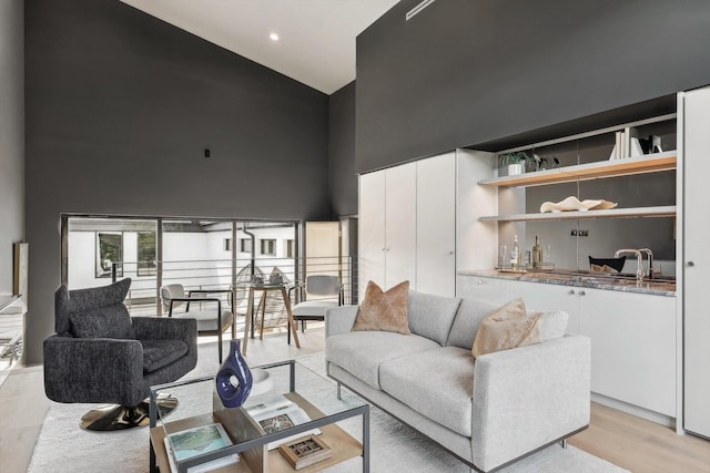 living room with sink, light wood-type flooring, and a high ceiling