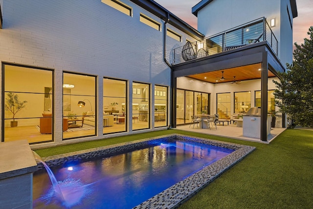 back house at dusk featuring a lawn, ceiling fan, a patio, pool water feature, and a balcony