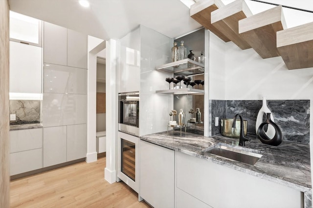 kitchen with sink, light stone countertops, beverage cooler, oven, and white cabinets