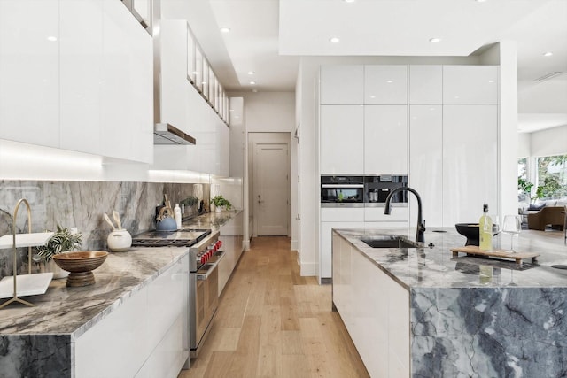 kitchen with high end range, sink, white cabinetry, and light stone counters