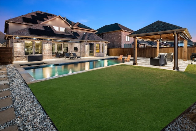 pool at dusk featuring a gazebo, a yard, an outdoor hangout area, and a patio