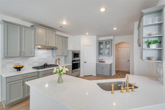 kitchen featuring light stone countertops, backsplash, gray cabinets, and stainless steel appliances