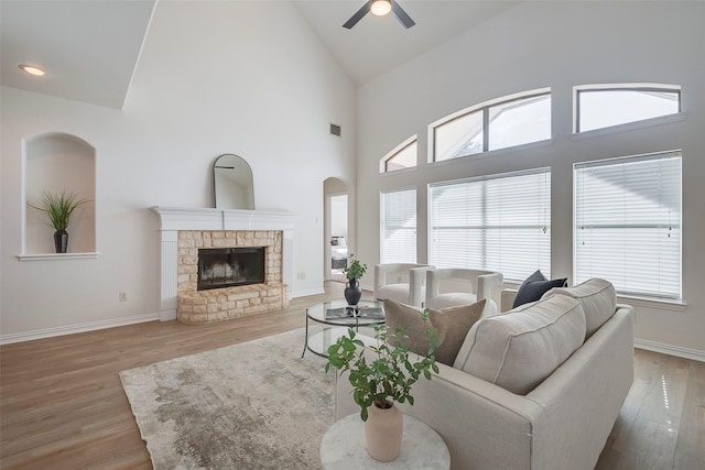 living room featuring ceiling fan, a stone fireplace, light hardwood / wood-style flooring, and high vaulted ceiling