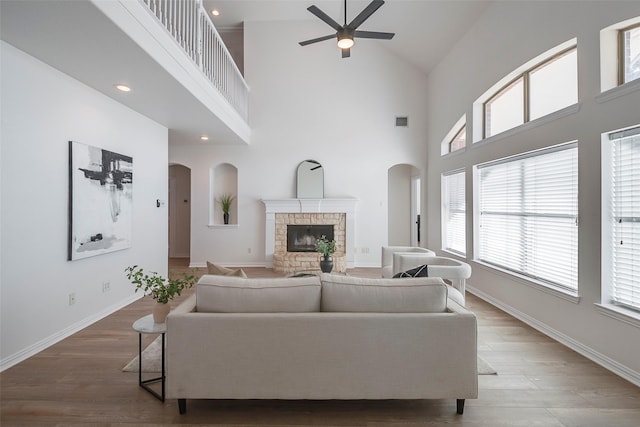 living room featuring ceiling fan, hardwood / wood-style floors, a towering ceiling, and a fireplace