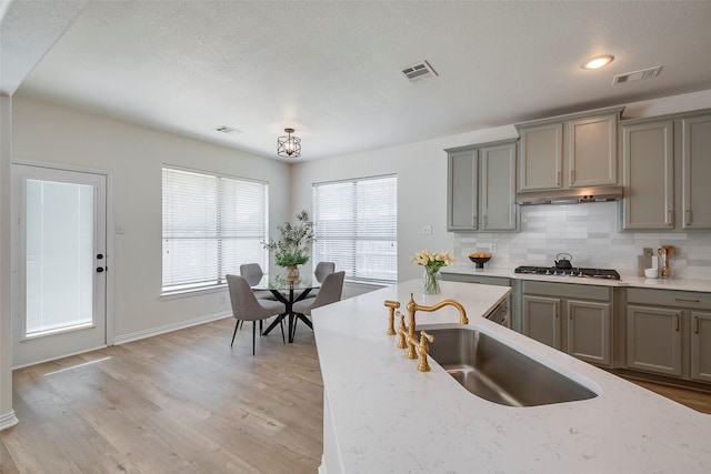 kitchen with sink, light wood-type flooring, tasteful backsplash, light stone counters, and stainless steel gas cooktop