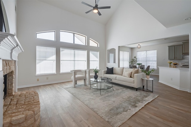 living room with ceiling fan, hardwood / wood-style floors, high vaulted ceiling, and a stone fireplace