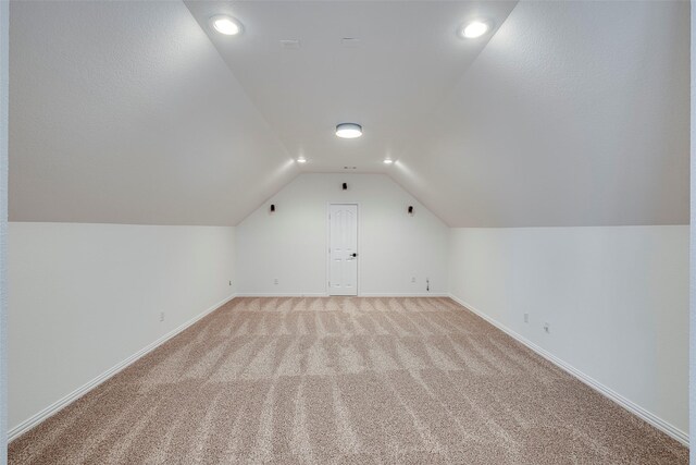 additional living space with light carpet and vaulted ceiling