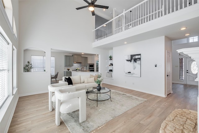 living room with plenty of natural light, light hardwood / wood-style flooring, a towering ceiling, and ceiling fan