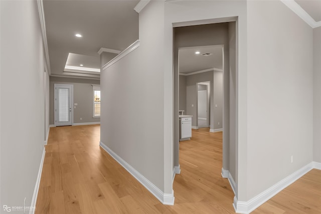 hall featuring light hardwood / wood-style flooring, ornamental molding, and a raised ceiling