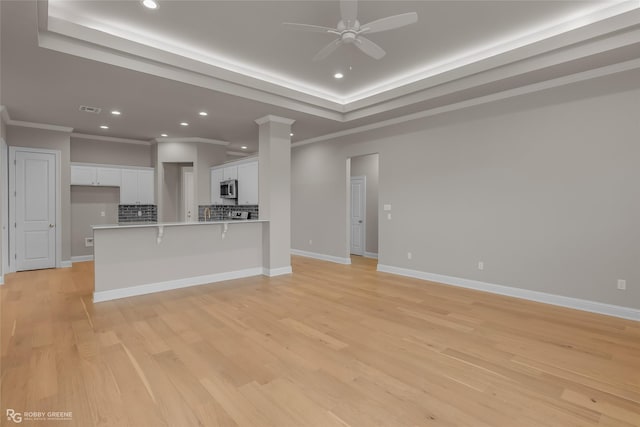 unfurnished living room with decorative columns, ornamental molding, a raised ceiling, ceiling fan, and light hardwood / wood-style floors