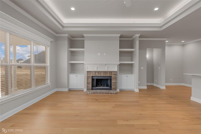 unfurnished living room featuring a brick fireplace, ornamental molding, a raised ceiling, and light wood-type flooring