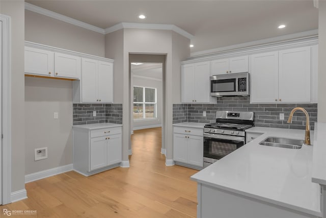 kitchen with sink, white cabinets, ornamental molding, stainless steel appliances, and light hardwood / wood-style flooring