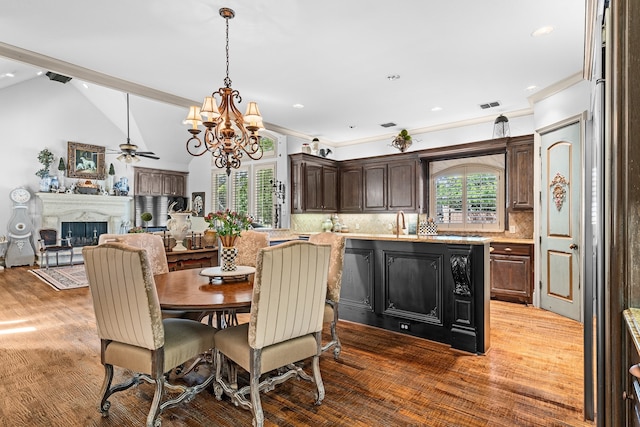 dining room with crown molding, hardwood / wood-style flooring, sink, vaulted ceiling, and ceiling fan with notable chandelier