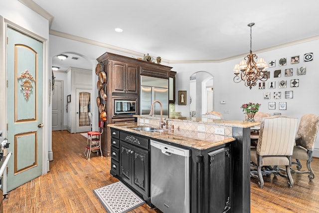 kitchen with built in appliances, a center island with sink, ornamental molding, and sink