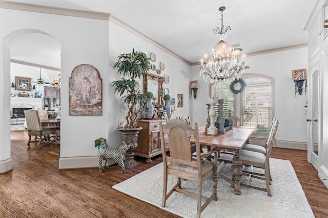 dining space featuring a fireplace, hardwood / wood-style flooring, ceiling fan with notable chandelier, and crown molding