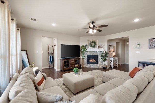 living room featuring ceiling fan, dark hardwood / wood-style floors, and a stone fireplace