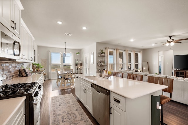 kitchen featuring white cabinets, stainless steel appliances, sink, hanging light fixtures, and a center island with sink