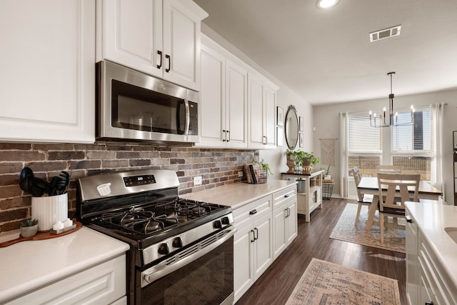 kitchen with appliances with stainless steel finishes, dark hardwood / wood-style floors, pendant lighting, white cabinets, and decorative backsplash