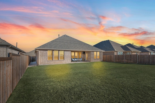 back house at dusk featuring a patio and a lawn