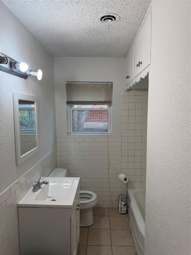 bathroom with tile patterned floors, toilet, tile walls, a textured ceiling, and vanity