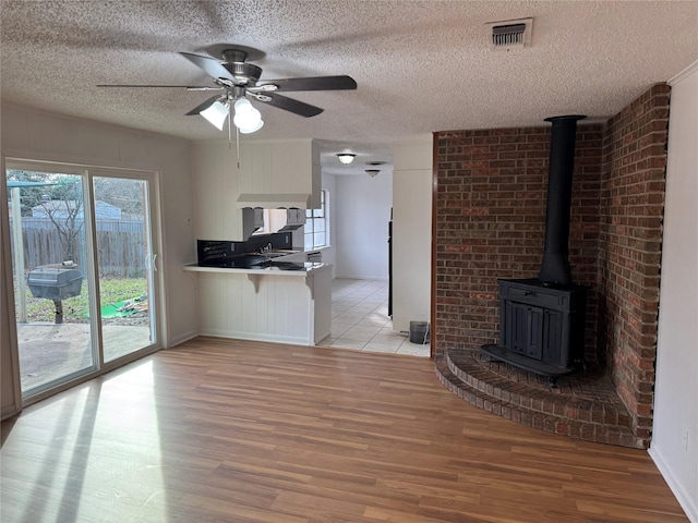 unfurnished living room featuring ceiling fan, a wood stove, a textured ceiling, and light hardwood / wood-style flooring