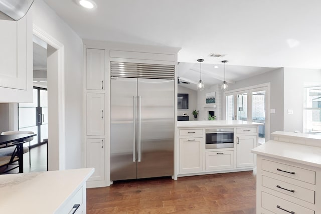 kitchen with lofted ceiling, appliances with stainless steel finishes, dark hardwood / wood-style floors, pendant lighting, and white cabinets