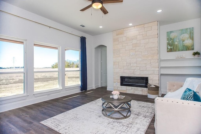 living room with ceiling fan, plenty of natural light, dark hardwood / wood-style flooring, and a stone fireplace