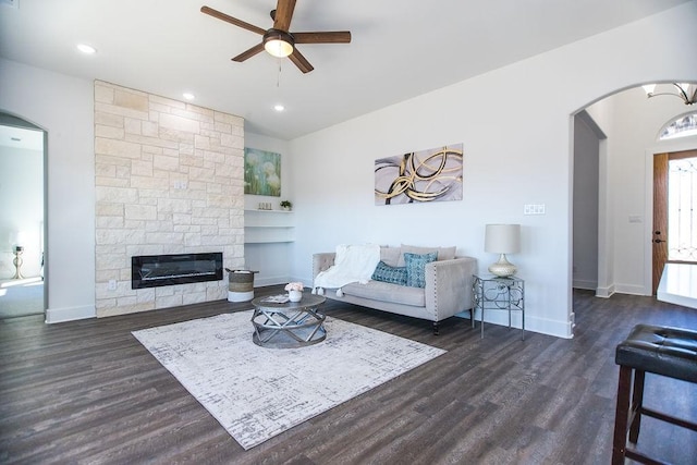 living room with ceiling fan, dark hardwood / wood-style floors, and a stone fireplace