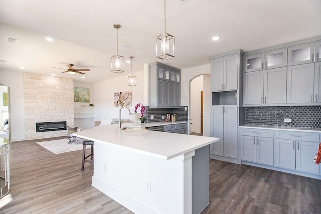 kitchen with light stone countertops, backsplash, hanging light fixtures, and sink