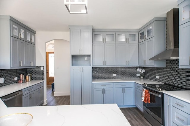 kitchen with light stone countertops, stainless steel appliances, wall chimney exhaust hood, and backsplash