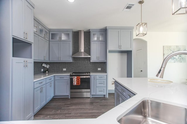 kitchen with wall chimney range hood, decorative light fixtures, stainless steel range with electric stovetop, backsplash, and light stone counters