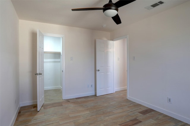 unfurnished bedroom featuring ceiling fan, a closet, a walk in closet, and light wood-type flooring