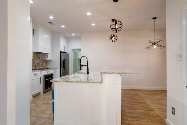 kitchen with white cabinetry, pendant lighting, backsplash, stainless steel appliances, and a center island with sink