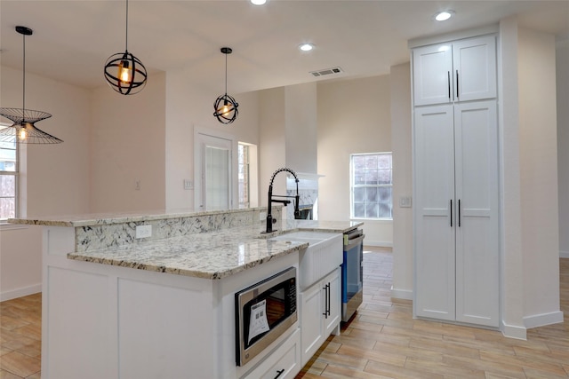 kitchen featuring light stone countertops, pendant lighting, a large island with sink, white cabinetry, and stainless steel appliances