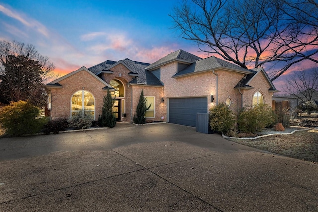 view of front of home featuring driveway, a shingled roof, a garage, and brick siding