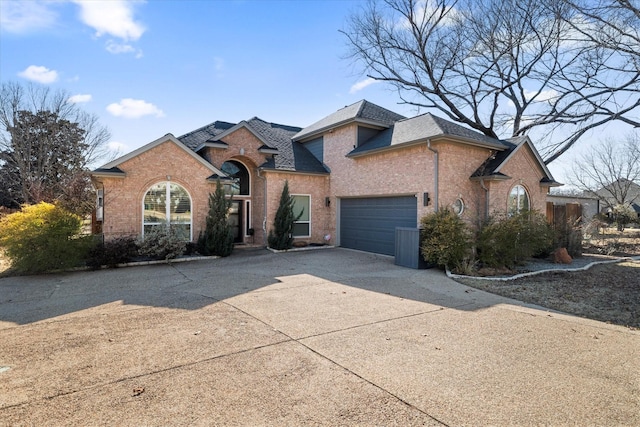 view of front facade featuring a garage, roof with shingles, concrete driveway, and brick siding