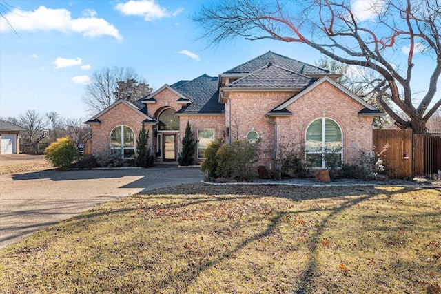 view of front facade featuring brick siding, a front yard, fence, and a shingled roof