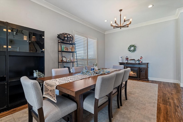 dining room featuring crown molding, an inviting chandelier, wood finished floors, a warm lit fireplace, and baseboards