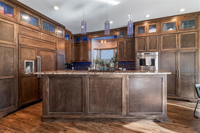 kitchen with light stone counters, oven, hanging light fixtures, a center island, and glass insert cabinets