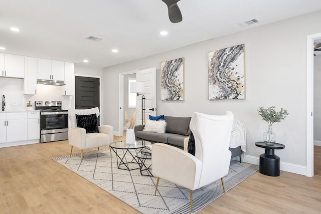 living room featuring ceiling fan, sink, and light hardwood / wood-style flooring