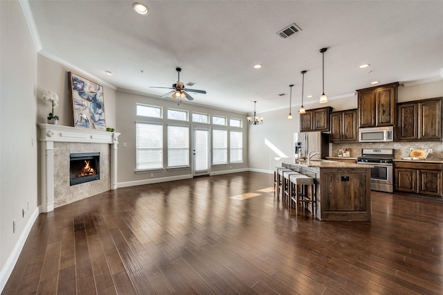 kitchen featuring light stone countertops, stainless steel appliances, an island with sink, a kitchen breakfast bar, and hanging light fixtures