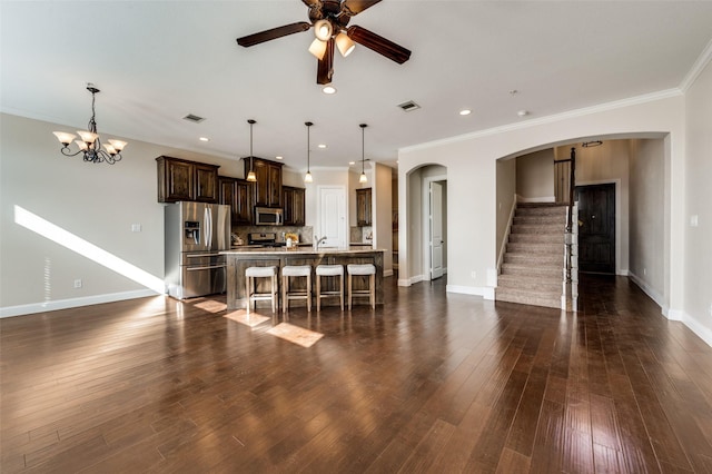 kitchen with crown molding, decorative light fixtures, an island with sink, a breakfast bar area, and stainless steel appliances