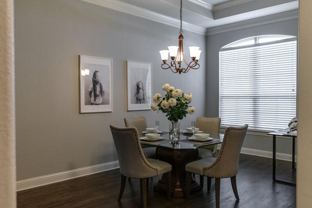 dining space featuring dark wood-type flooring, a tray ceiling, ornamental molding, and an inviting chandelier