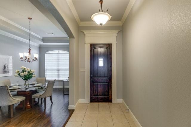 entryway with light tile patterned floors, crown molding, and a chandelier