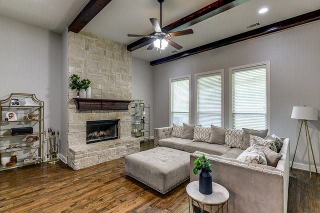 living room featuring ceiling fan, dark hardwood / wood-style floors, beam ceiling, and a stone fireplace