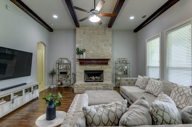 living room with a fireplace, dark hardwood / wood-style floors, beamed ceiling, and ceiling fan