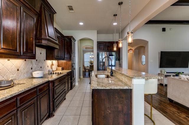 kitchen with decorative light fixtures, black electric stovetop, sink, a center island with sink, and a breakfast bar area