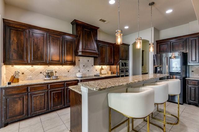 kitchen with a center island, hanging light fixtures, stainless steel fridge, light stone counters, and custom range hood